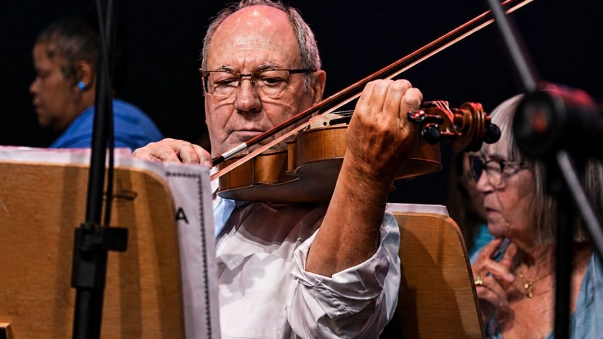 Aluno idoso toca violino em apresentação da Orquestra Master
