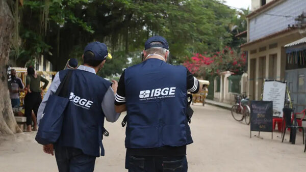 Agentes do IBGE uniformizados caminham por rua durante pesquisa domiciliar de campo