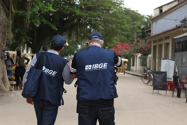 Agentes do IBGE uniformizados caminham por rua durante pesquisa domiciliar de campo