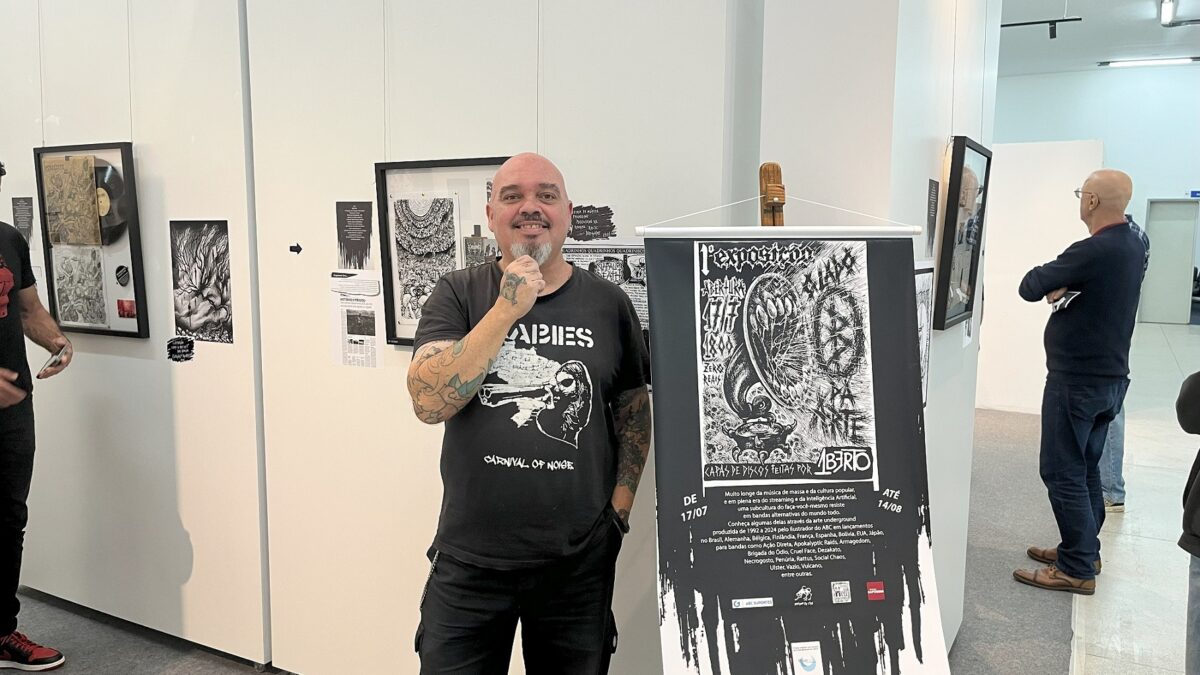 Ilustrador Umberto Daros ao lado de cartaz da exposição O Lado B da Arte em São Caetano