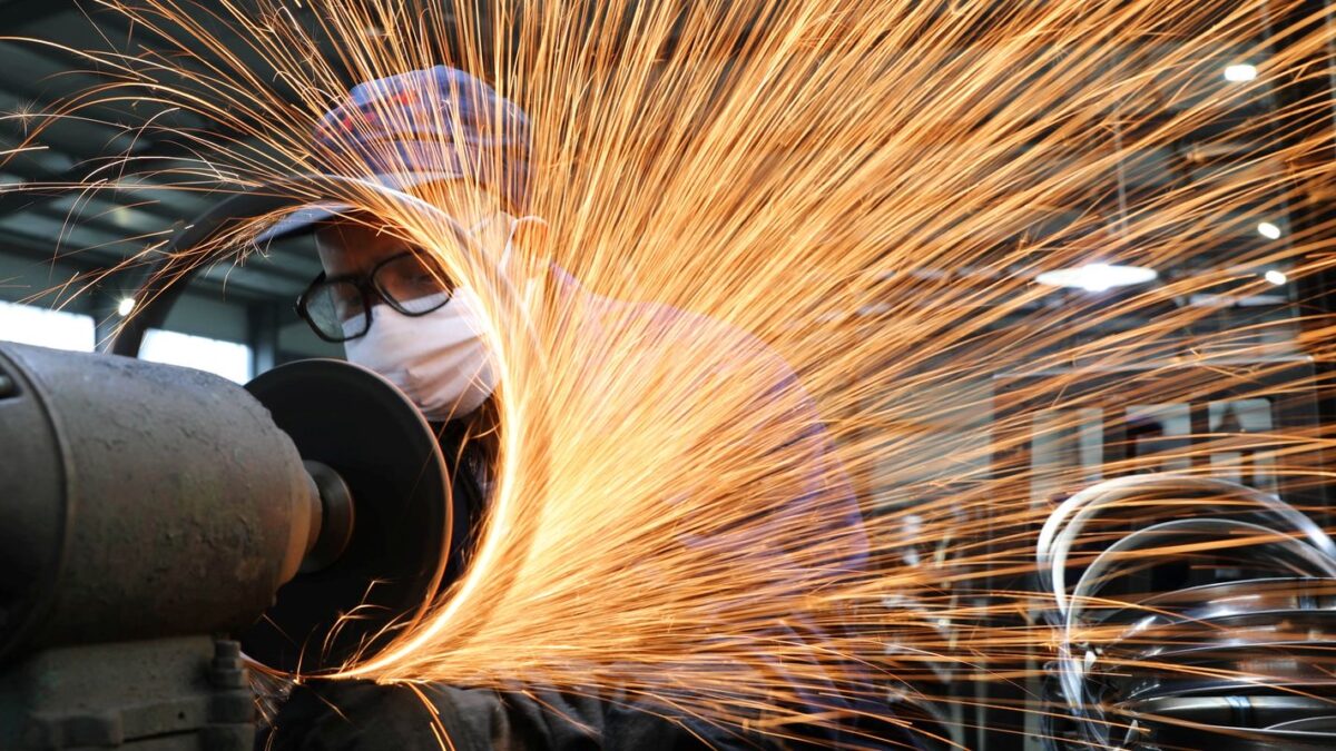 Trabalhador com máscara de proteção operando máquina em usina siderúrgica com faíscas de metal