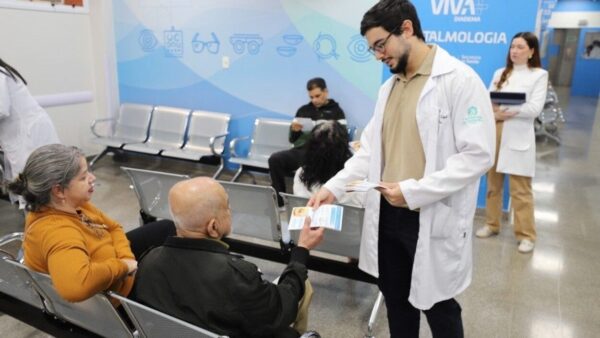 Médico entregando panfletos educativos sobre Doença do Olho Seco para pacientes idosos em sala de espera de unidade de saúde em Diadema