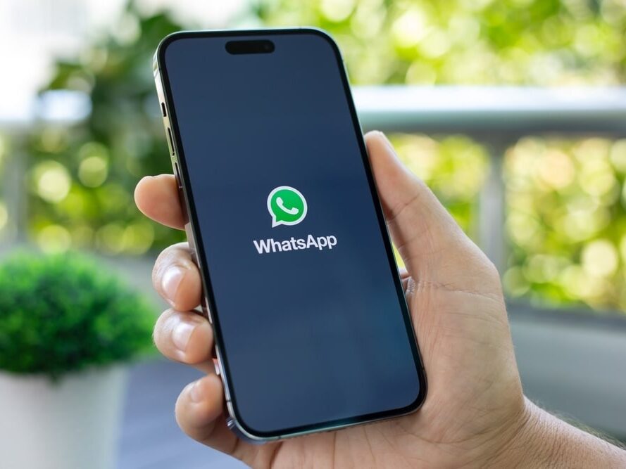 Mão segura celular exibindo tela de abertura do aplicativo WhatsApp
