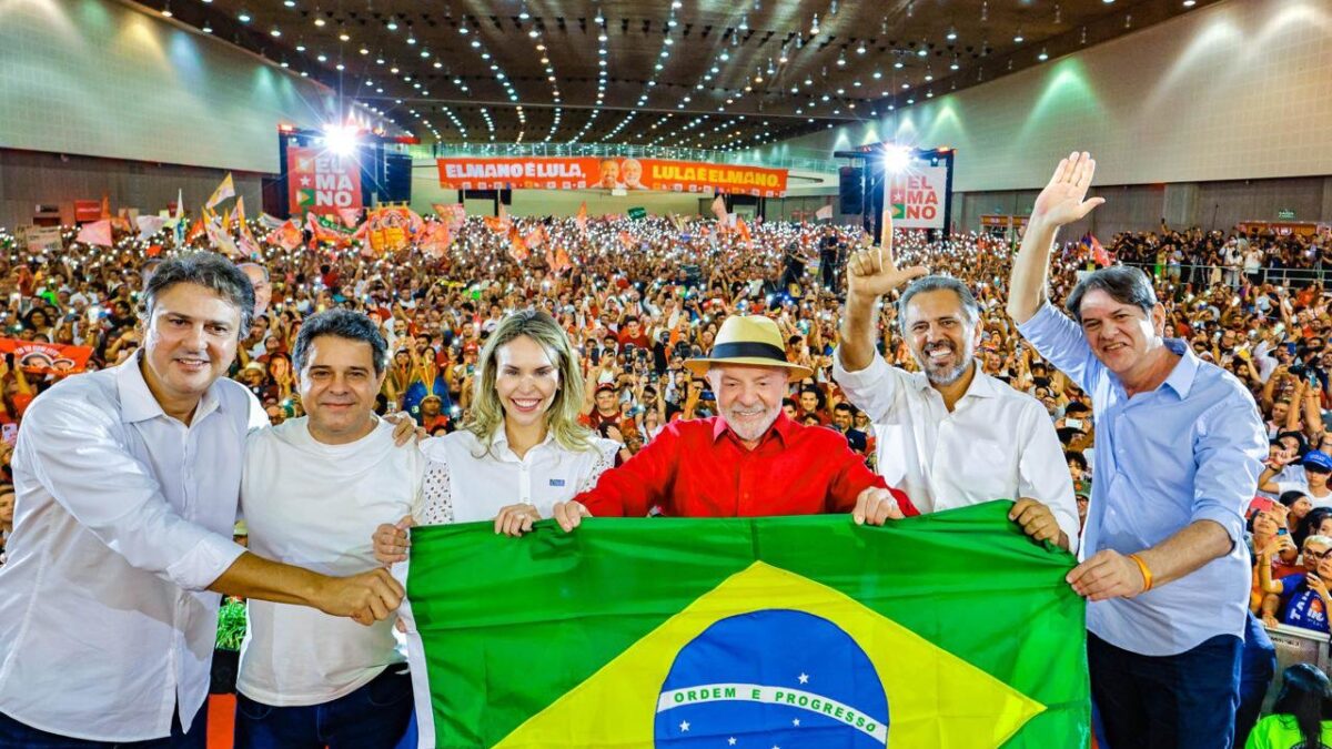 Lula, Elmano de Freitas e outras autoridades seguram bandeira do Brasil em palco de convenção com multidão ao fundo no Ceará