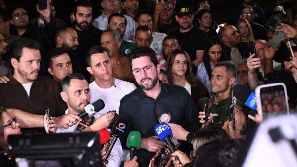 Político fala a jornalistas cercado de apoiadores e microfones durante entrevista coletiva à noite