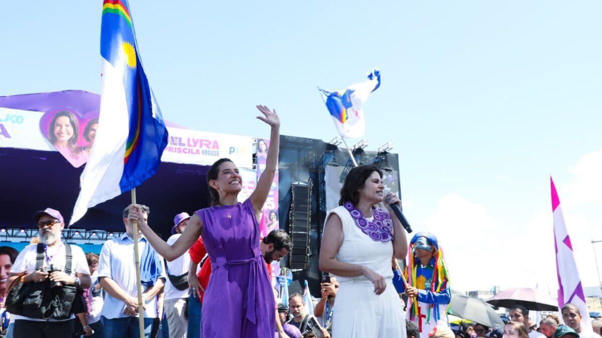 Raquel Lyra acenando ao lado de Priscila Krause em palco durante convenção partidária ao ar livre em Pernambuco