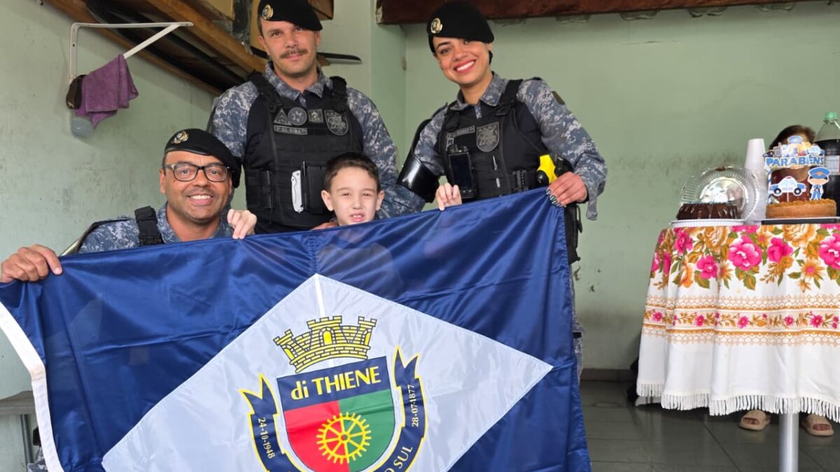 Guardas civis municipais e menino Theo seguram a bandeira de São Caetano do Sul em festa de aniversário