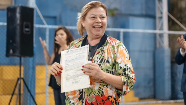 Moradora sorridente segura escritura de imóvel durante entrega em São Bernardo
