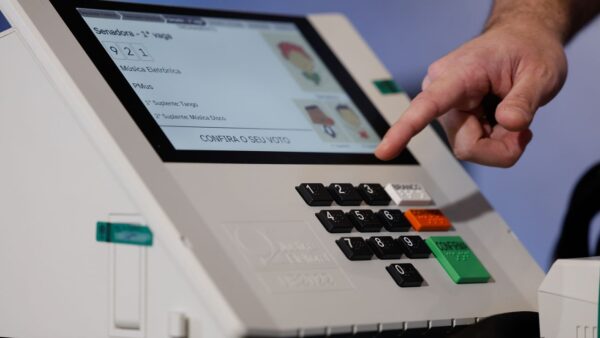 Dedo pressiona tela de urna eletrônica confirmando voto