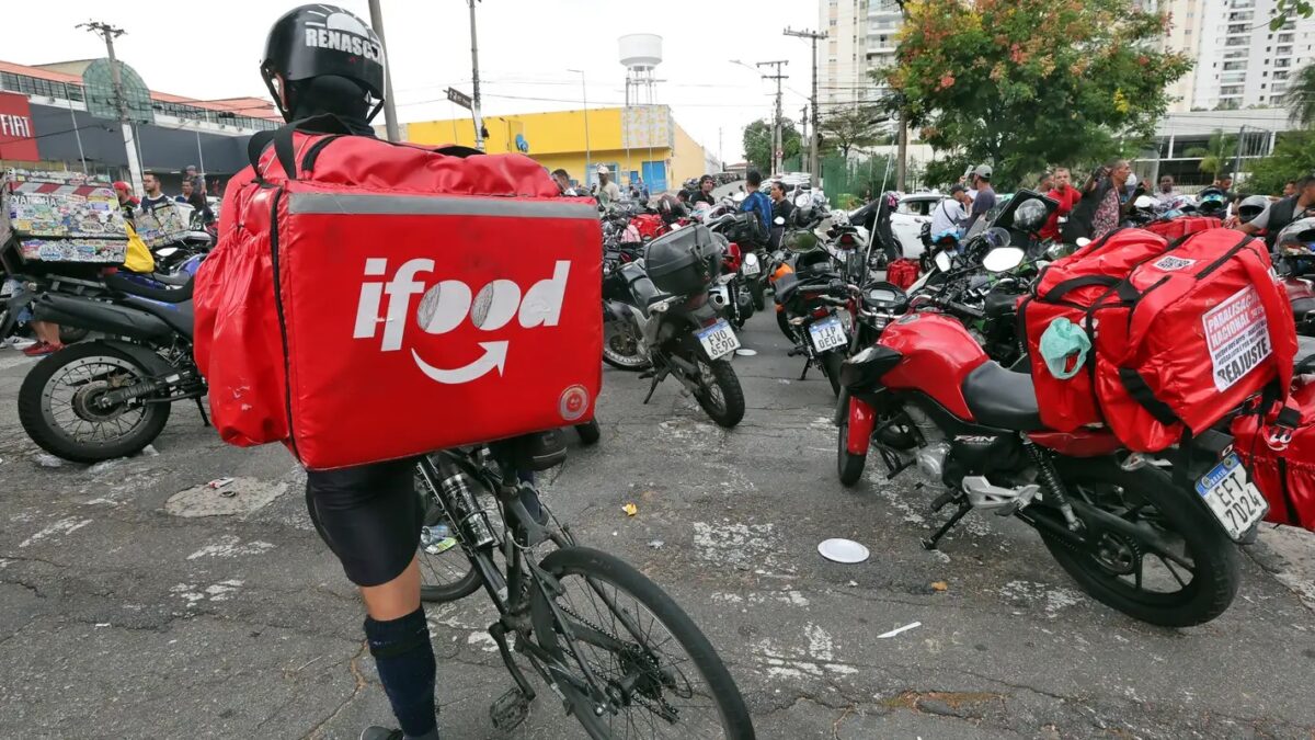 Entregador de bicicleta com bolsa térmica do iFood em meio a motociclistas na rua
