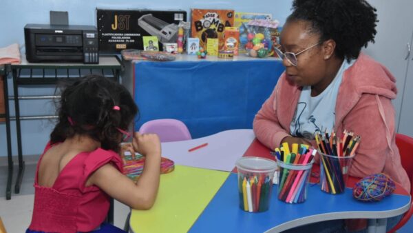 Criança e educadora em mesa com materiais pedagógicos em sala de recursos multifuncionais
