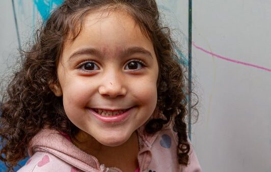Criança sorridente em frente a mural colorido na EMEB Eremita Gonçalves da Costa reformada em Diadema