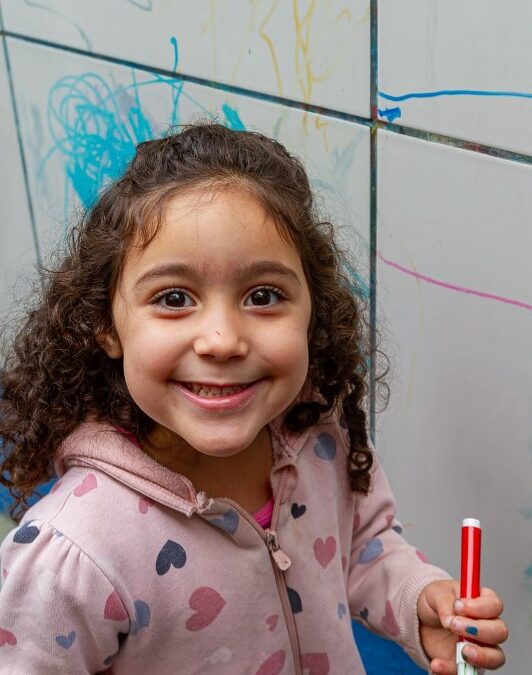 Criança sorridente em frente a mural colorido na EMEB Eremita Gonçalves da Costa reformada em Diadema