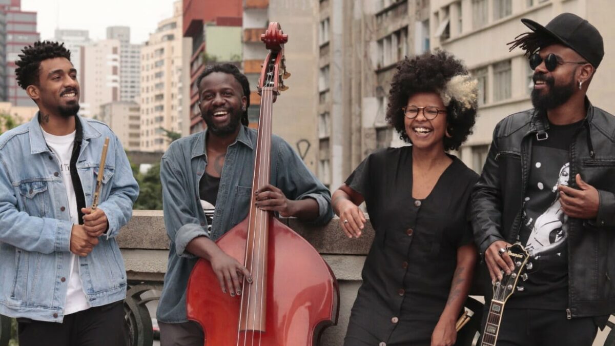 Integrantes do coletivo Adinkrazz sorrindo com instrumentos musicais em terraço