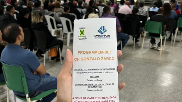 Morador segura folheto informativo sobre regularização fundiária durante reunião comunitária em Santo André