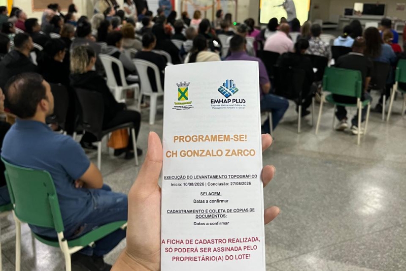 Morador segura folheto informativo sobre regularização fundiária durante reunião comunitária em Santo André