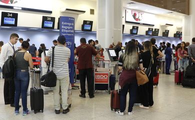 Passageiros com bagagem em fila de check-in em aeroporto