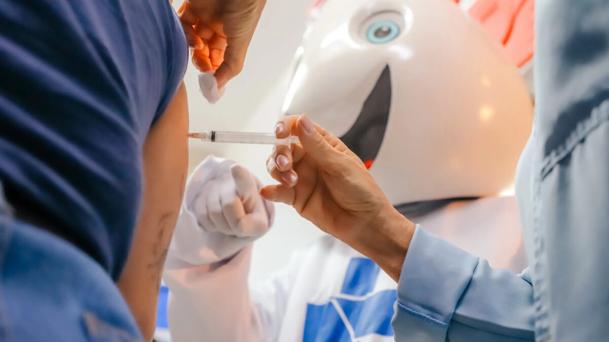 Profissional de saúde aplica vacina contra o sarampo ao lado do mascote Zé Gotinha