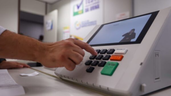 Dedo pressiona teclado de urna eletrônica durante teste de segurança