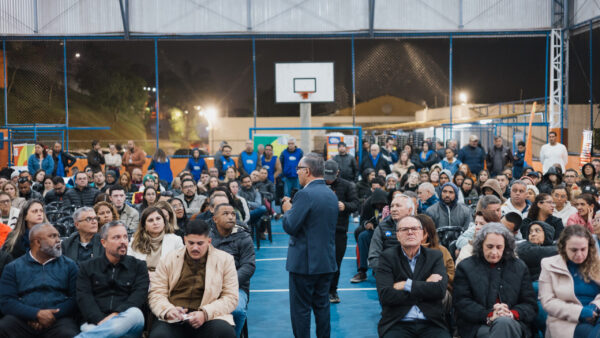 Prefeito fala ao microfone para plateia sentada em quadra durante encontro Voz da Gente