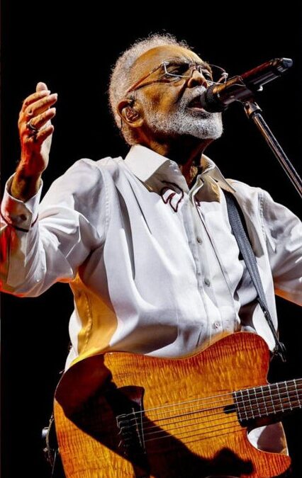 Gilberto Gil tocando guitarra e cantando ao microfone em show