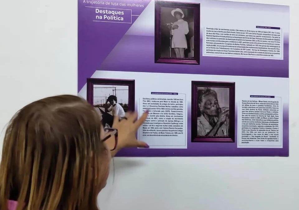 Criança observando painel de exposição sobre trajetória de luta das mulheres no Paço Municipal de Mauá