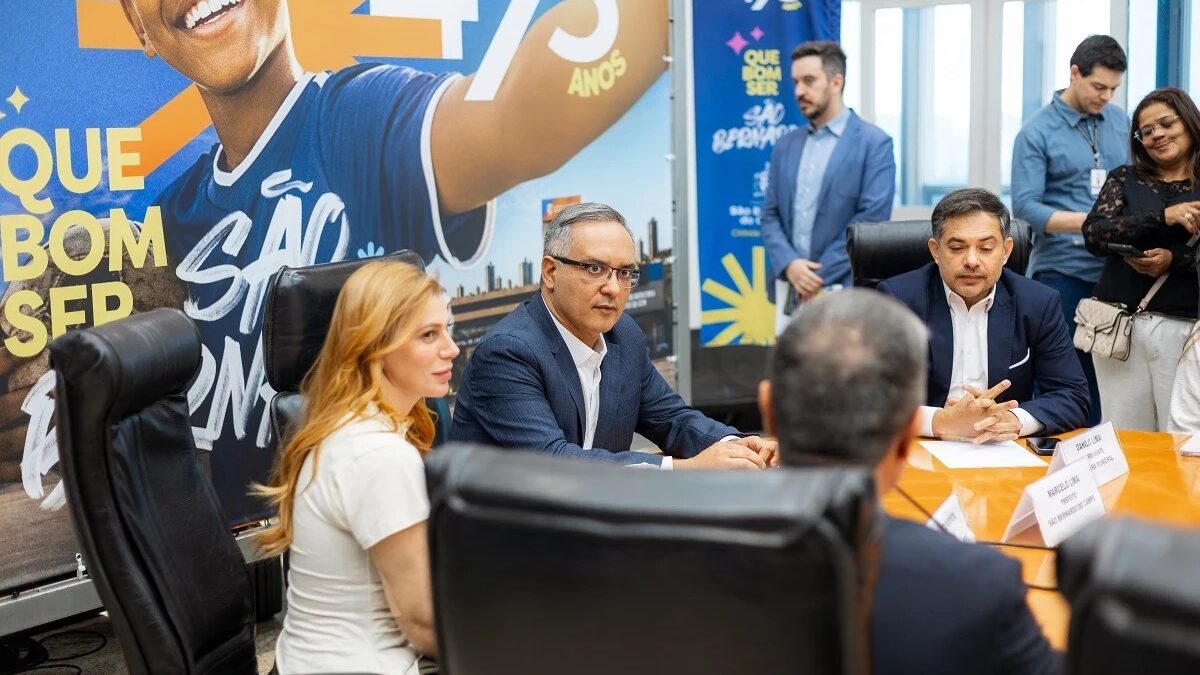 Prefeito Marcelo Lima em coletiva de imprensa sentado à mesa com banner de aniversário de 473 anos de São Bernardo ao fundo