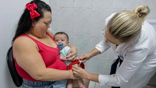 Profissional de saúde aplica vacina em bebê no colo da mãe