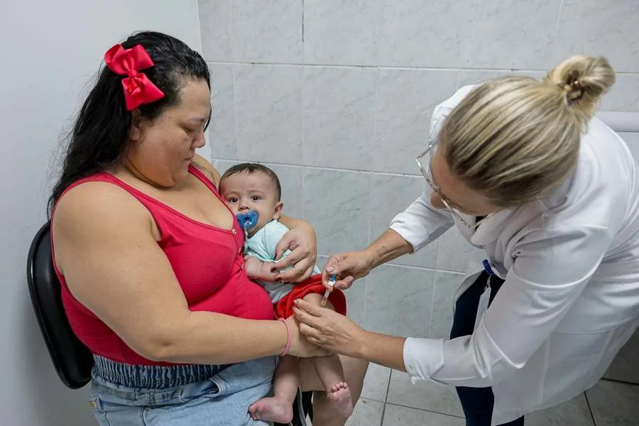 Profissional de saúde aplica vacina em bebê no colo da mãe