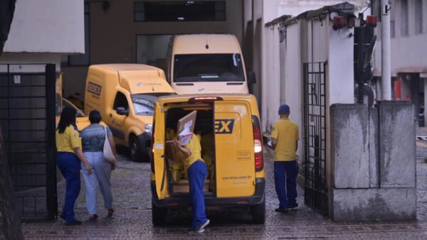 Funcionários dos Correios carregam veículo de entregas em frente a agência