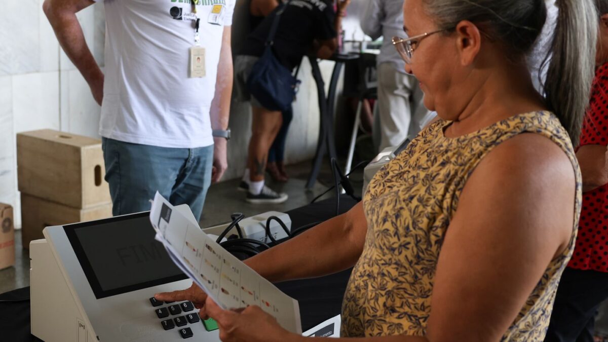 Eleitora consulta cola eleitoral em papel antes de votar em urna eletrônica