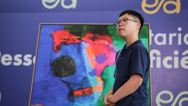 Artista Henrique Yasuhiro ao lado de uma de suas telas na exposição Hey.wa no Paço Municipal