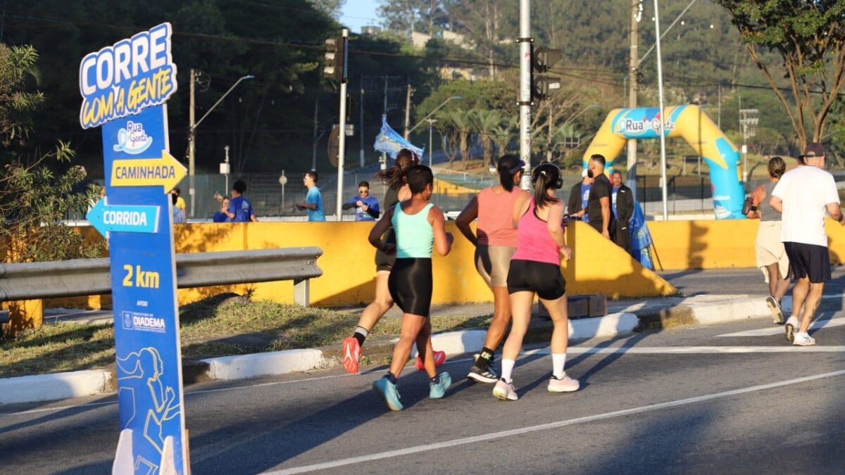 Corredores passam por placa do Corre com a Gente, com indicação de corrida e caminhada, durante o Rua da Gente em Diadema