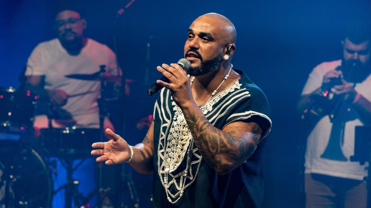 O cantor Dilemba durante show, com integrantes da banda ao fundo (foto de apresentação anterior, divulgação / acervo Dilemba)