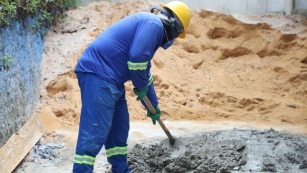 Trabalhador da construção civil prepara massa de cimento com pá durante atividade de alvenaria