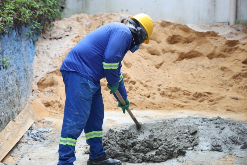 Trabalhador da construção civil prepara massa de cimento com pá durante atividade de alvenaria